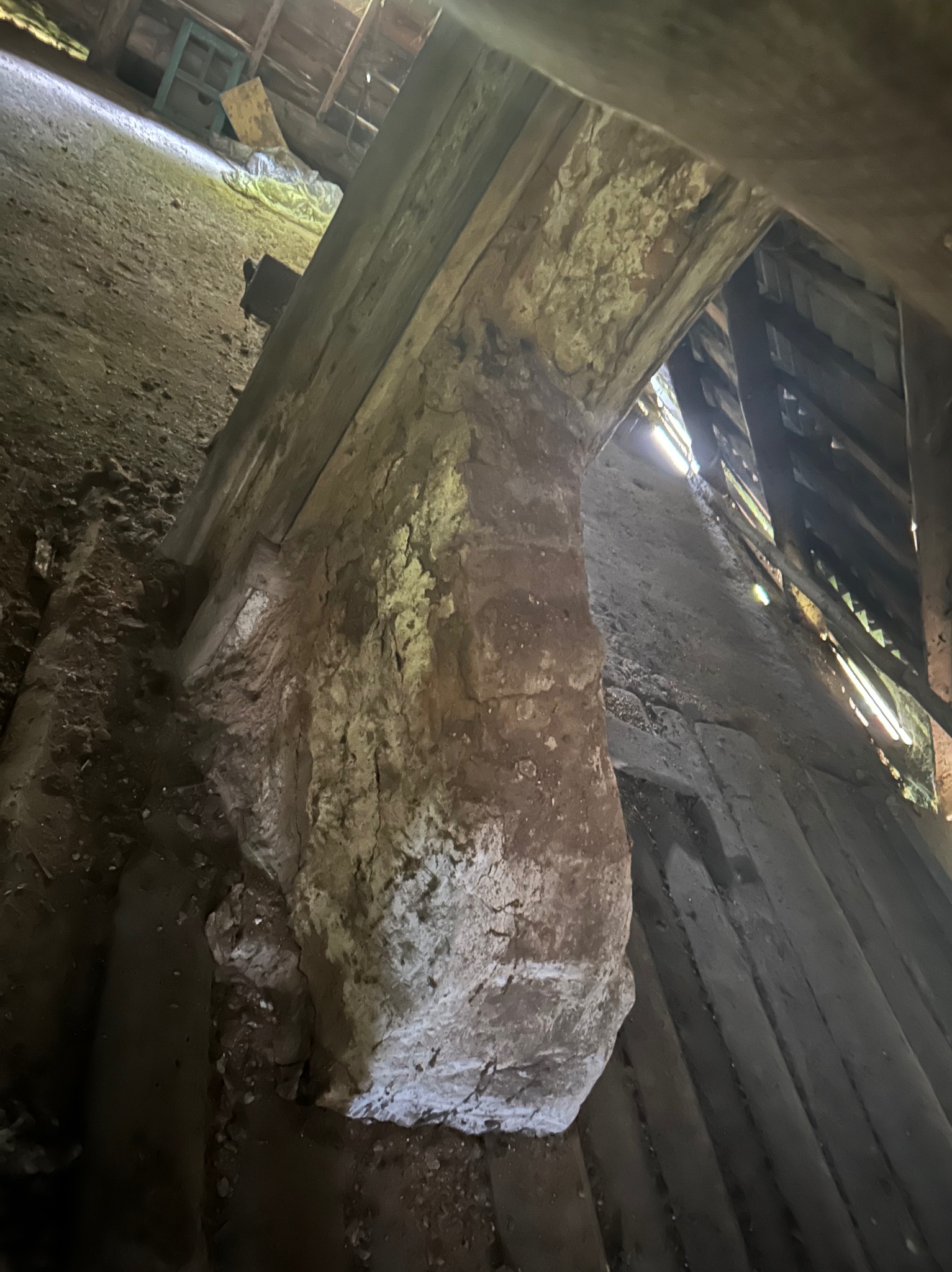 Wnętrze starego, zaniedbanego budynku z fragmentami muru i drewnianej konstrukcji. Widoczne ślady zniszczeń i upływu czasu, surowa faktura materiałów.