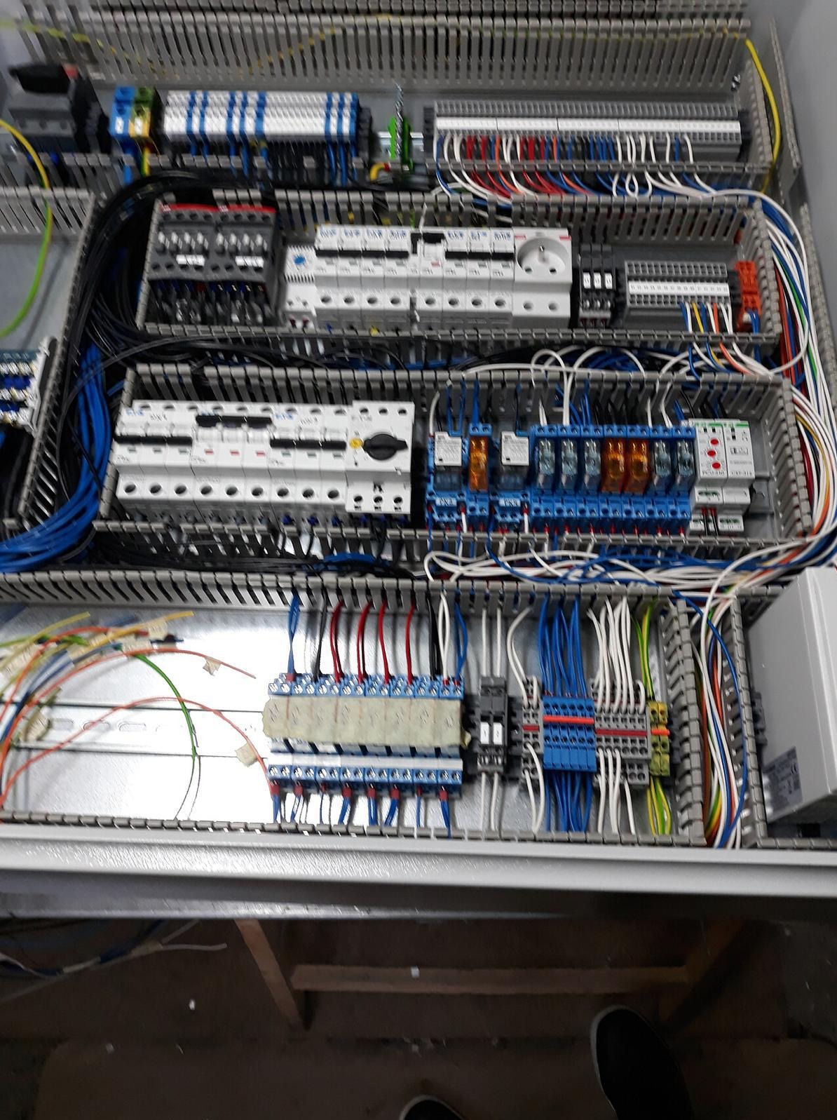 Rozdzielnica elektryczna z licznymi przewodami, przekaźnikami i zabezpieczeniami, widok z góry. Precyzyjne połączenia i uporządkowany układ komponentów.