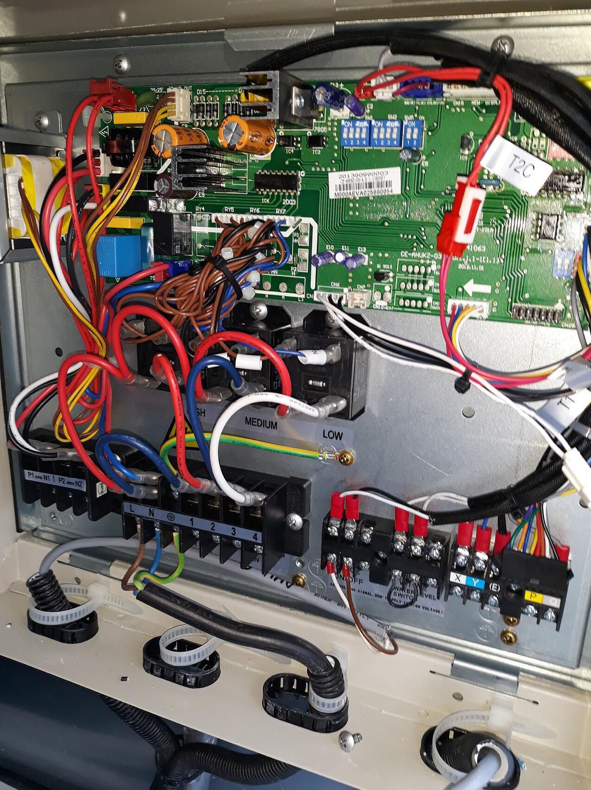 Wnętrze skrzynki sterowniczej z widoczną płytą główną, licznymi przewodami w kolorach czerwonym, niebieskim i białym oraz złączkami elektrycznymi.