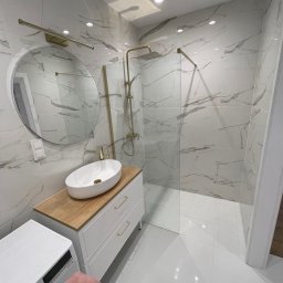 K&V SEVKO SPÓŁKA Z OGRANICZONĄ ODPOWIEDZIALNOŚCIĄ - Nowoczesna łazienka z kabiną prysznicową typu walk-in, umywalką nablatową na szafce i okrągłym lustrem. Białe płytki imitujące marmur z delikatnym złotym akcentem.