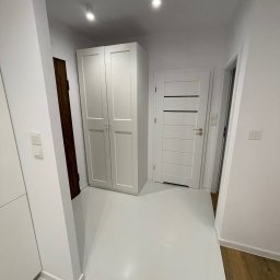 K&V SEVKO SPÓŁKA Z OGRANICZONĄ ODPOWIEDZIALNOŚCIĄ - Białe wnętrze korytarza z szafą, drzwiami i błyszczącą podłogą. Widoczne detale wykończenia, takie jak listwy przypodłogowe i włączniki światła.