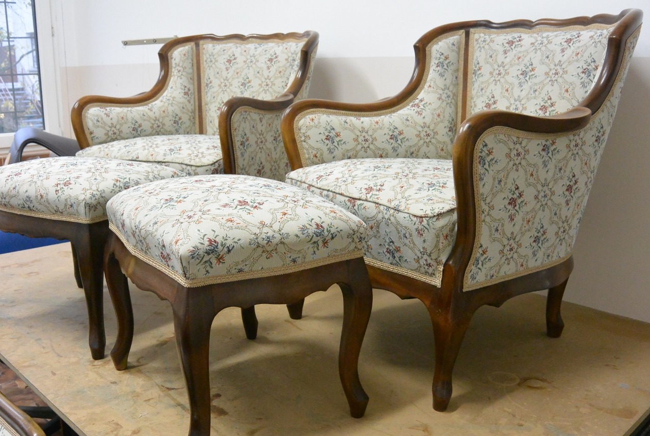 Dwa fotele i podnóżki z tapicerką w kwiaty i drewnianymi elementami, ustawione obok siebie. Widoczne detale wykończenia i wzór tapicerki. Klasyczny styl.
