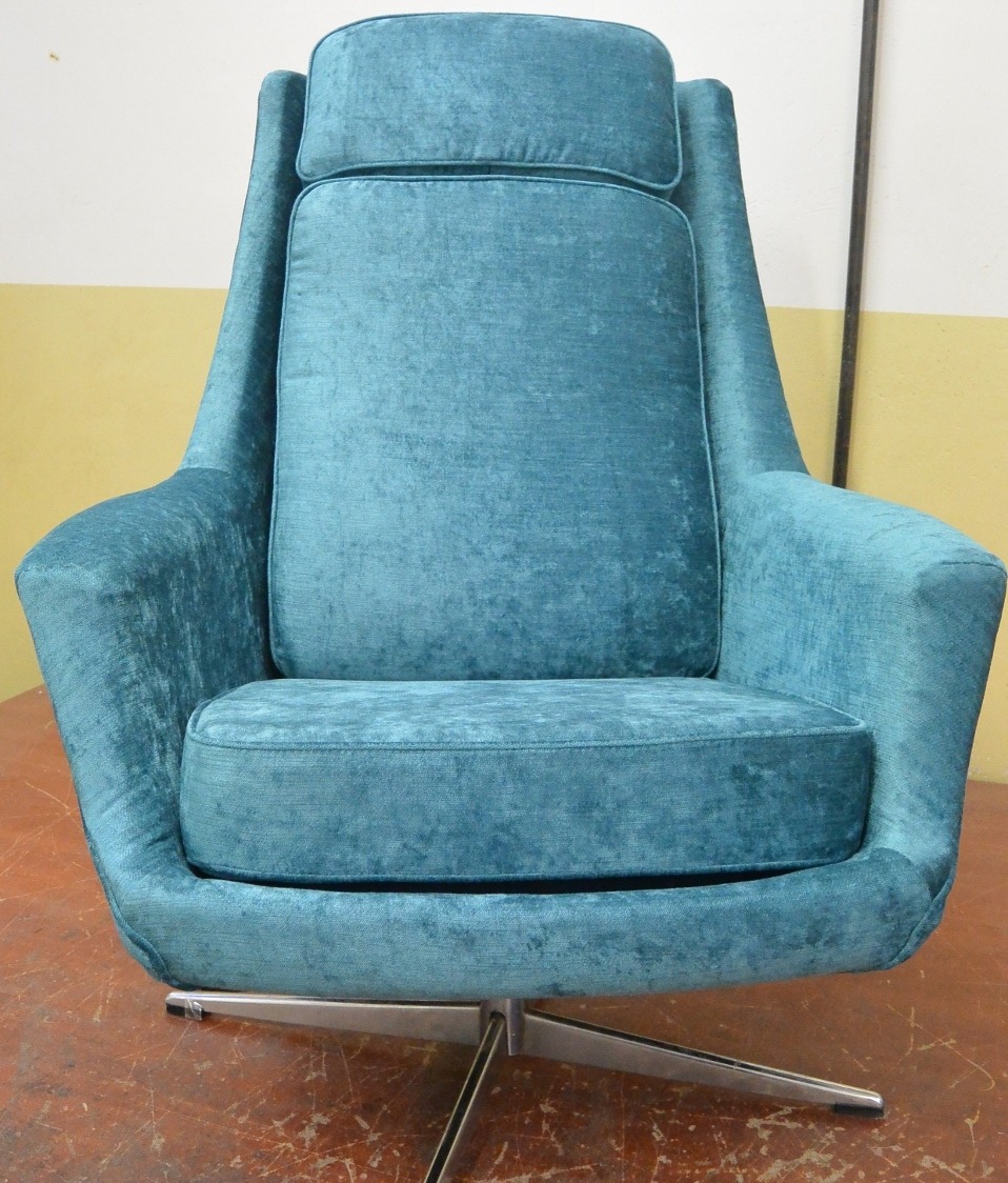 Turkusowy fotel obrotowy z wysokim oparciem i zagłówkiem, tapicerowany welurem, na metalowej podstawie krzyżakowej. Widok z przodu, na tle ściany.