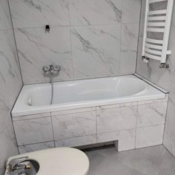 Jarosław zieliński - Wykończona łazienka w bieli i szarości: wanna obudowana płytkami imitującymi marmur, grzejnik drabinkowy i bidet. Minimalistyczny styl, świeżo po remoncie.