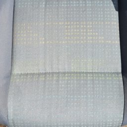 Janek Nowrocki - Wyczyszczone siedzisko samochodowe z delikatnym wzorem w odcieniach szarości i błękitu, widoczne ślady prania, fragment buta na dywaniku. Efekt po praniu tapicerki.