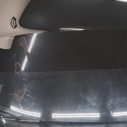 Janek Nowrocki - Błyszcząca, czarna karoseria auta z widocznymi śladami polerowania i odbiciem osoby. Refleksy świetlne podkreślają gładkość powierzchni po zabiegu detailingu.