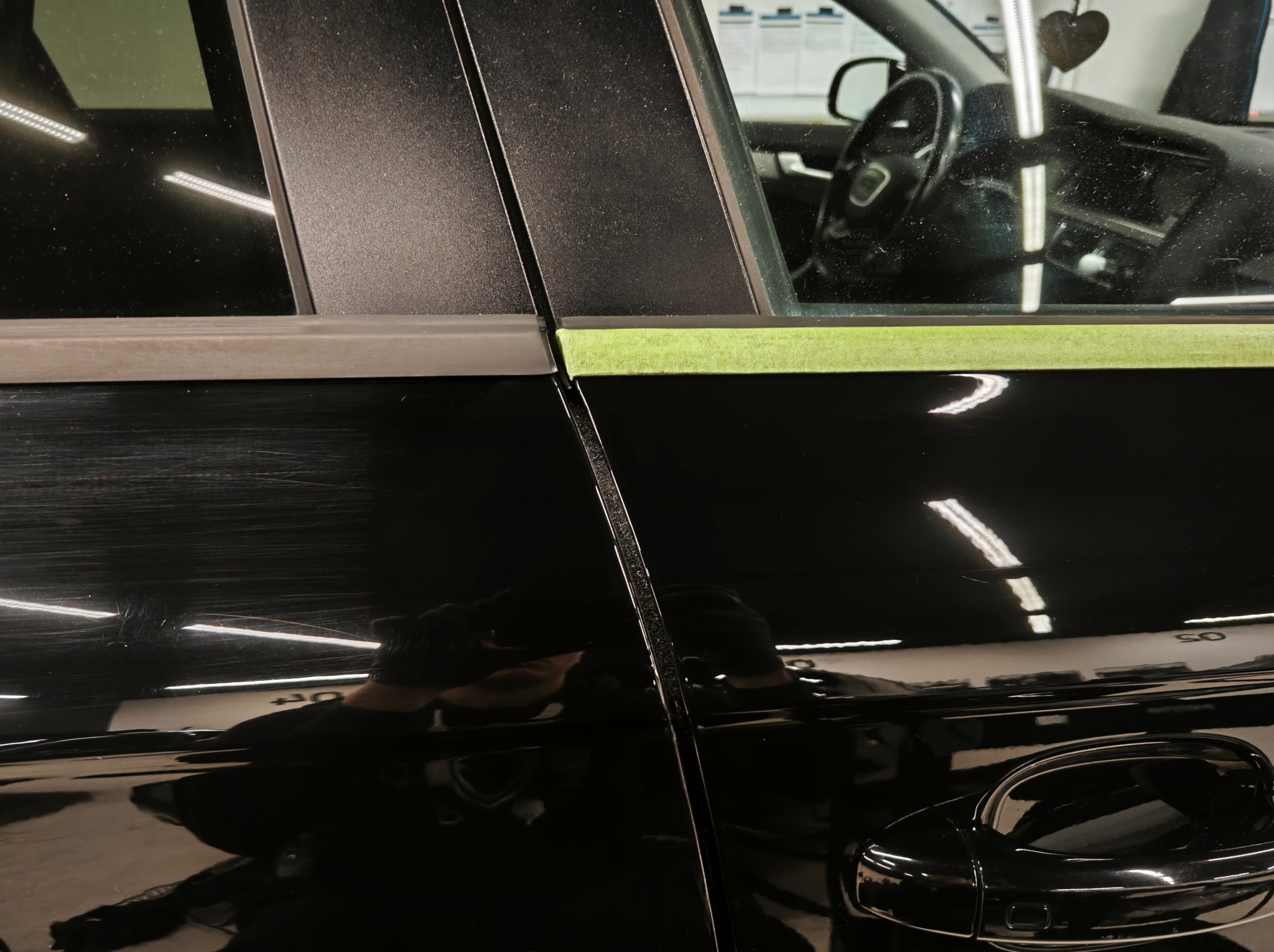 Czarne auto z rysami na lakierze, zabezpieczone taśmą malarską przed polerowaniem. Widoczne odbicie osoby wykonującej usługę.
