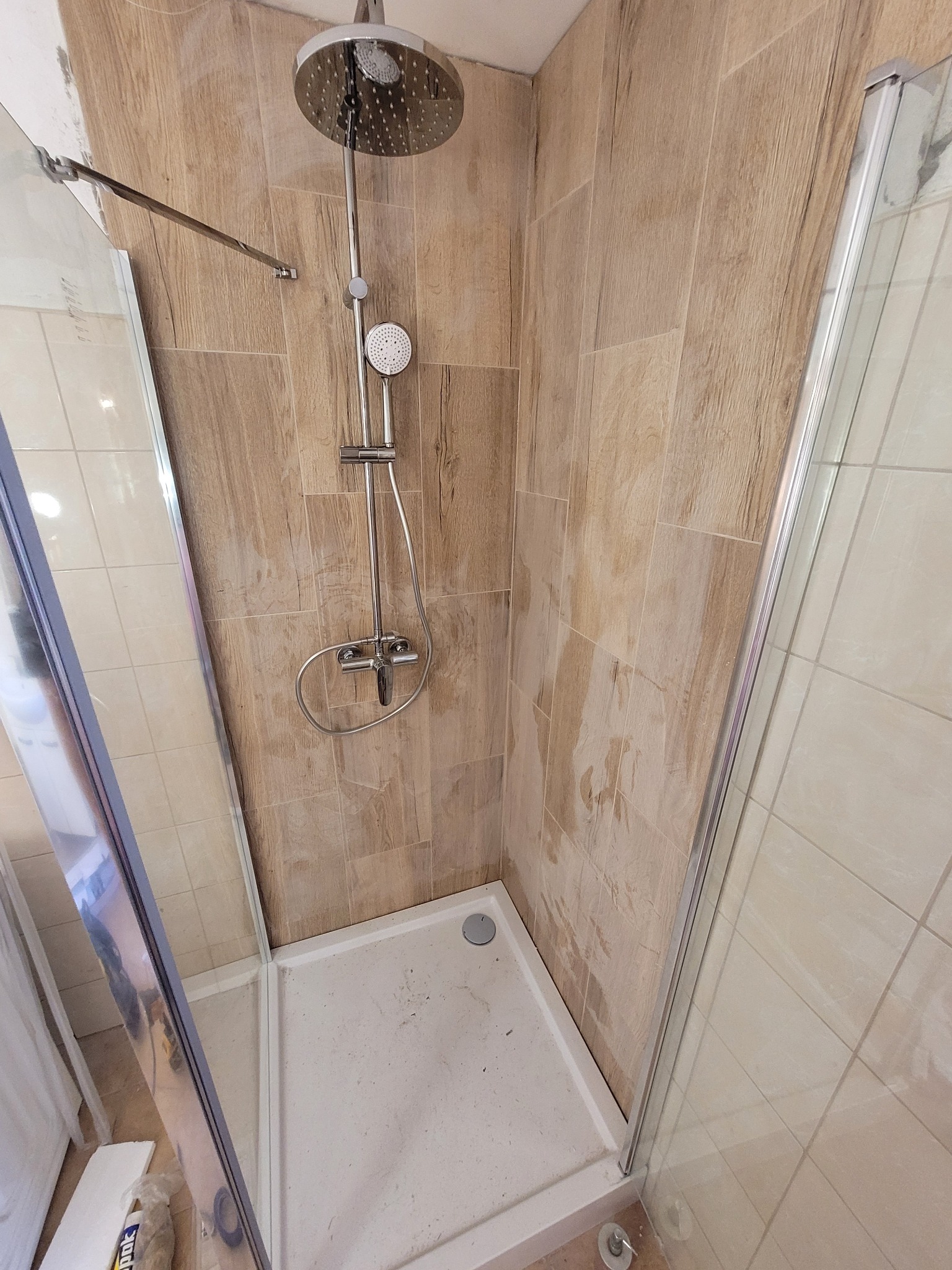 Kabina prysznicowa z deszczownicą i panelami ściennymi imitującymi drewno. Widoczne detale wykończenia i armatura. Ujęcie z perspektywy wnętrza kabiny.