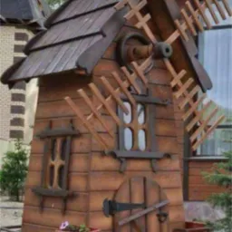 Drewniana konstrukcja w kształcie wiatraka z oknami i drzwiami, umieszczona w ogrodzie. Dekoracyjny element architektury ogrodowej, wykonany z brązowego drewna.