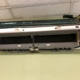 Zdemontowany, brudny klimatyzator ścienny w trakcie serwisu. Widoczne zanieczyszczenia na elementach wewnętrznych i obudowie. Otwarta konstrukcja ukazuje stan przed czyszczeniem.