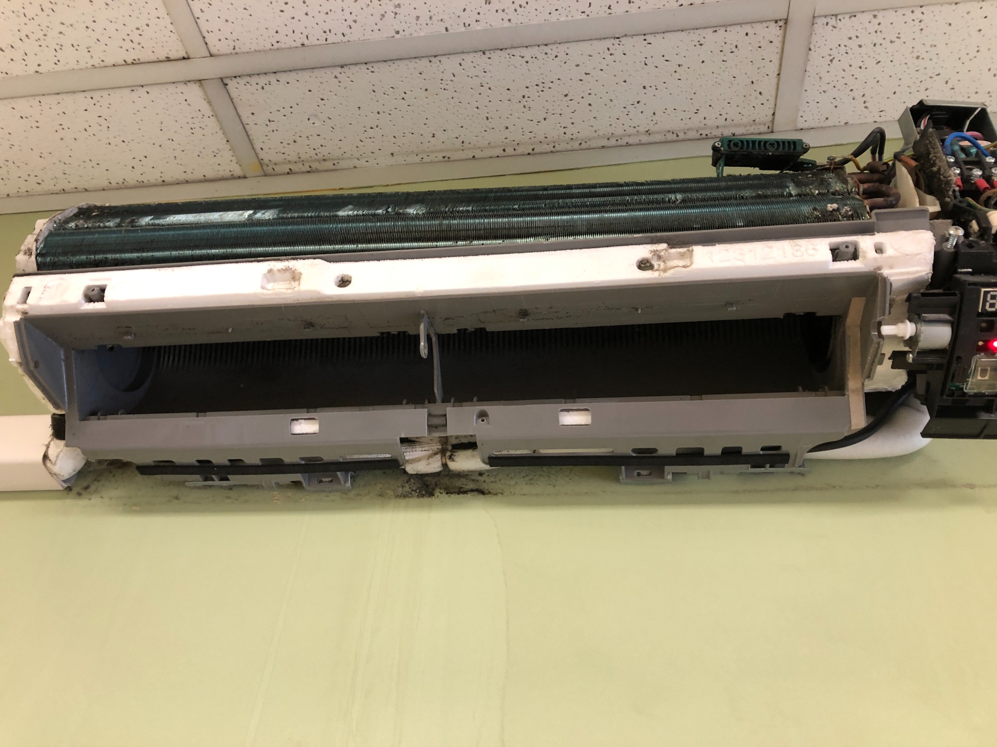 Zdemontowany, brudny klimatyzator ścienny w trakcie serwisu. Widoczne zanieczyszczenia na elementach wewnętrznych i obudowie. Otwarta konstrukcja ukazuje stan przed czyszczeniem.