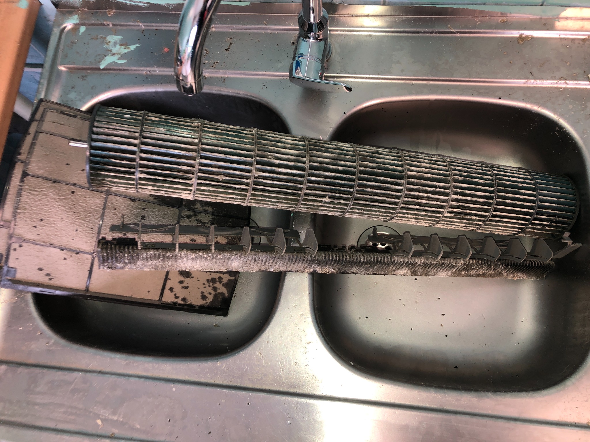 Brudny filtr i walec klimatyzacji w zlewie, widoczne osady i zanieczyszczenia. Elementy w trakcie czyszczenia lub przygotowania do serwisu. Kran w tle.