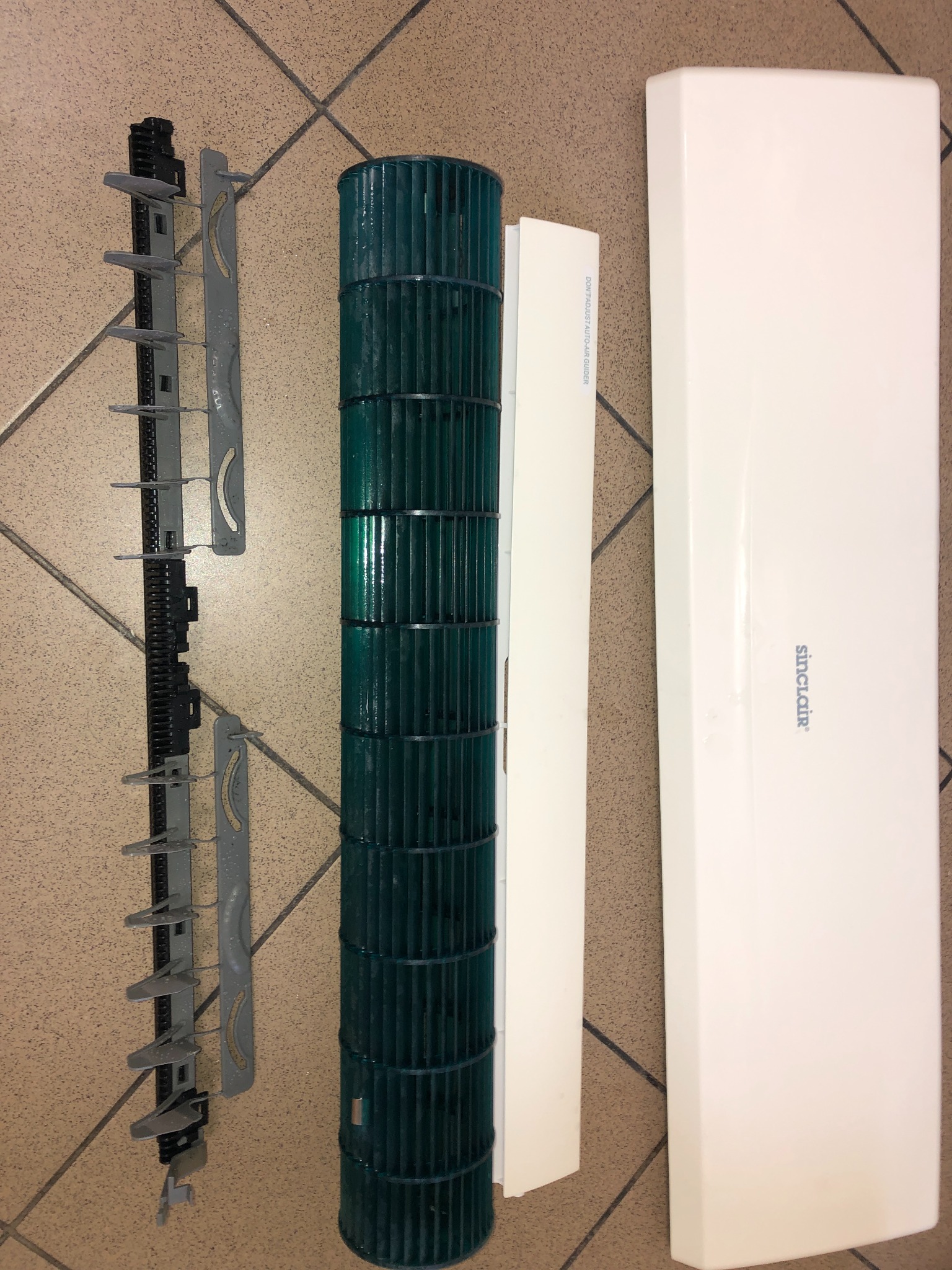 Rozłożone elementy klimatyzacji Sinclair: obudowa, filtr, wentylator bębnowy i prowadnice powietrza na brązowym tle. Widok z góry, detale konstrukcyjne.