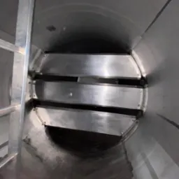 Wnętrze metalowej konstrukcji cylindrycznej z trzema poziomymi, metalowymi przegrodami. Widoczna drabina po lewej stronie. Spawy i nity łączą elementy.