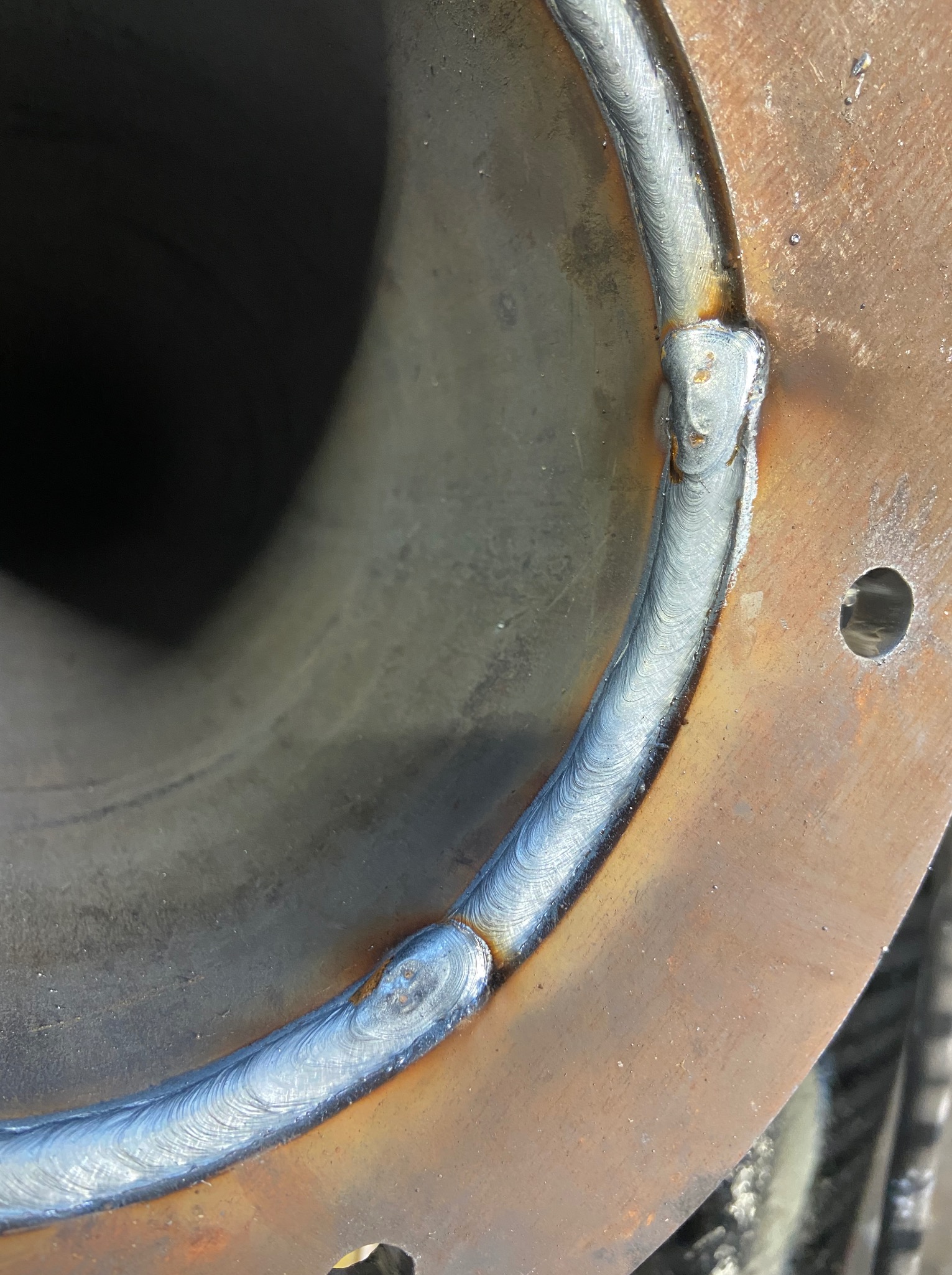 Spoina okrężna na złączu rury i kołnierza, wykonana metodą spawania łukowego. Widoczne ślady obróbki i ciepła na metalu.