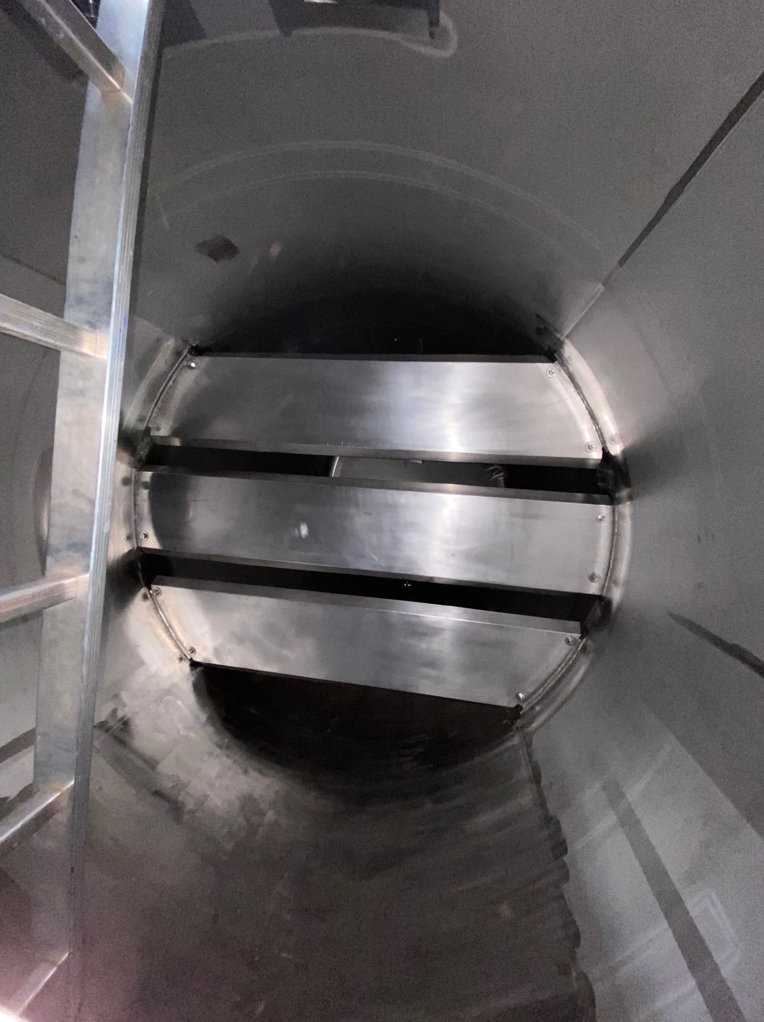 Wnętrze metalowej konstrukcji cylindrycznej z trzema poziomymi, metalowymi przegrodami. Widoczna drabina po lewej stronie. Spawy i nity łączą elementy.