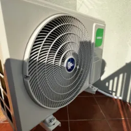 Zamontowana jednostka zewnętrzna klimatyzacji Kaisai na balkonie, widoczne mocowania i przew&oacute;d odprowadzający skropliny, cień rzucany przez balustradę.