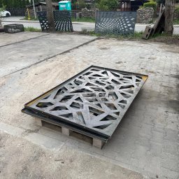 Profesjonalne cięcie CNC - Metalowy panel dekoracyjny z ażurowym wzorem geometrycznym, ułożony na palecie na zewnątrz, prawdopodobnie element ogrodzenia lub balustrady.