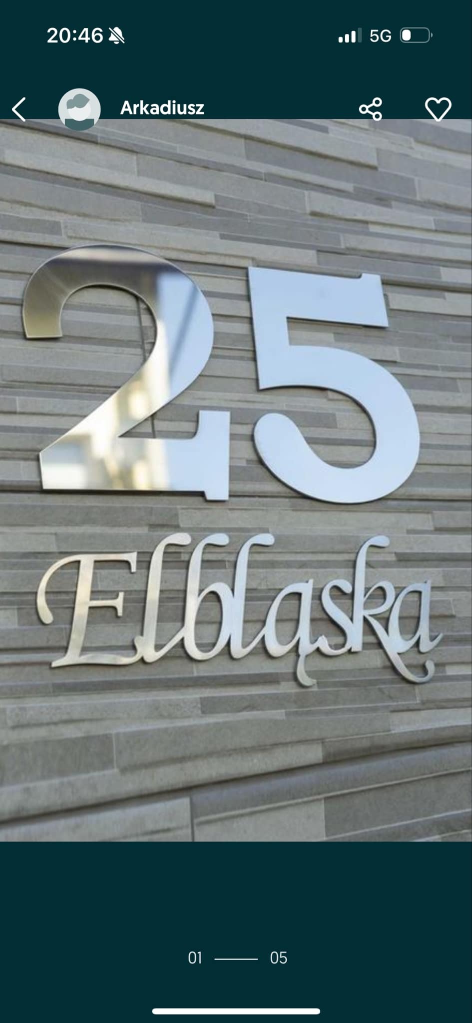 Adres domu: numer '25' i nazwa ulicy 'Elbląska', wykonane ze stali nierdzewnej, zamontowane na elewacji z szarej cegły. Elegancki i nowoczesny design.