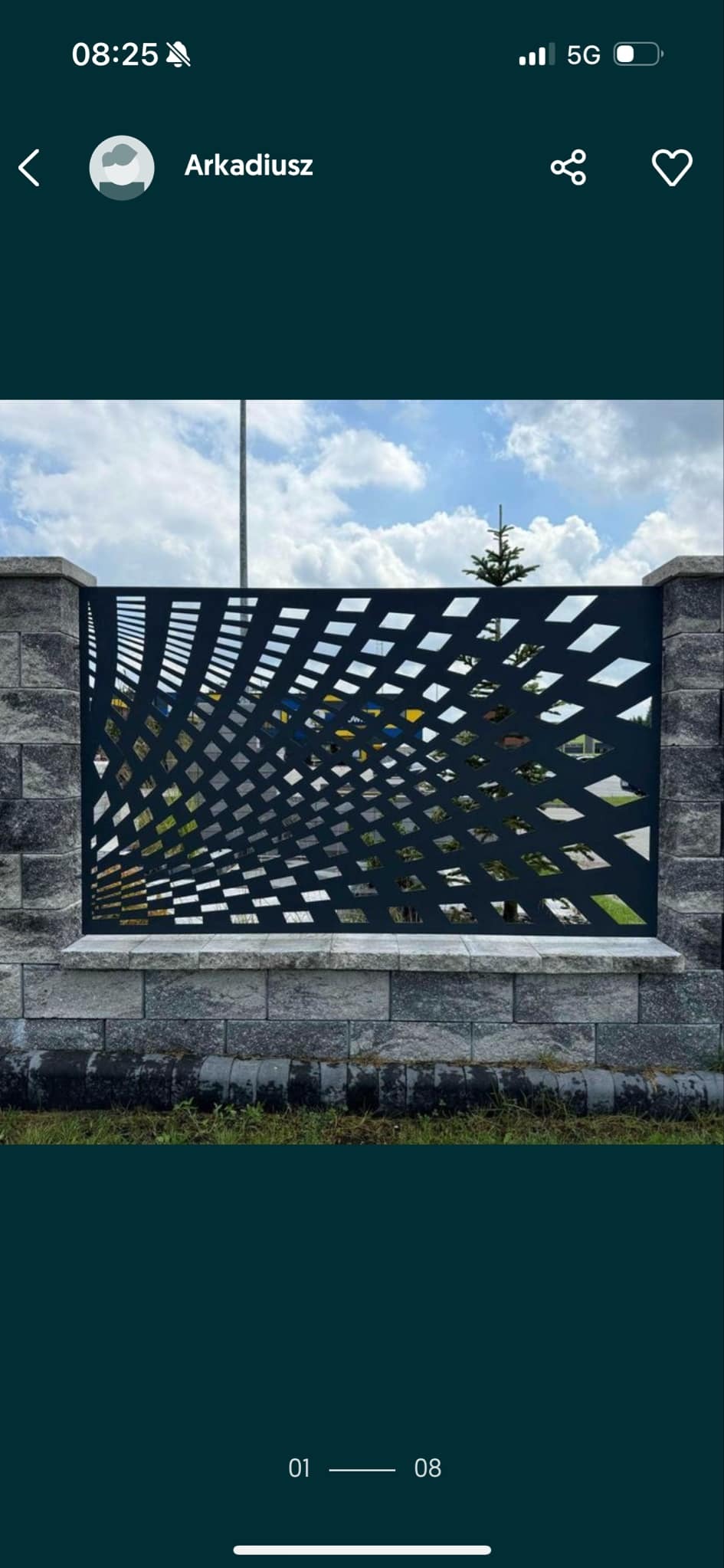 Nowoczesne ogrodzenie z metalu o geometrycznym wzorze, osadzone na kamiennej podmurówce. Widoczne niebo i zieleń w tle.