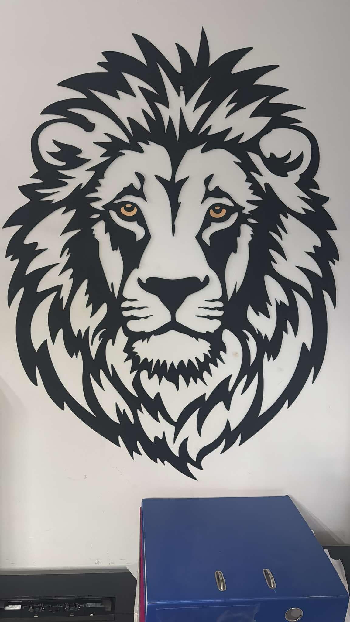 Czarna, metalowa dekoracja ścienna: głowa lwa z żółtymi oczami, umieszczona nad niebieskimi segregatorami. Wykonanie CNC.