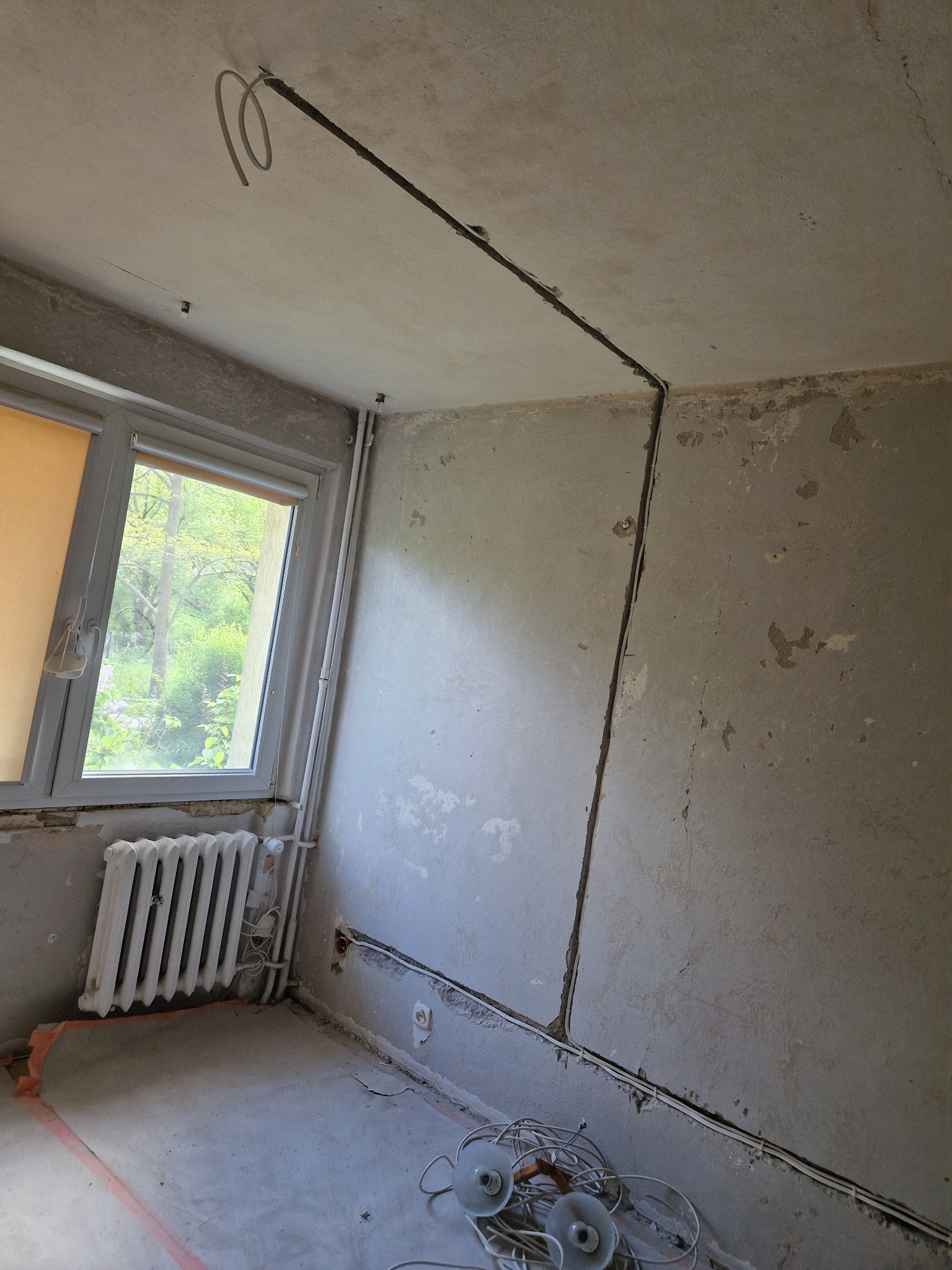 Wnętrze w trakcie remontu. Widoczne kable elektryczne prowadzone po ścianach i suficie, przygotowane do instalacji. Surowe ściany i podłoga.