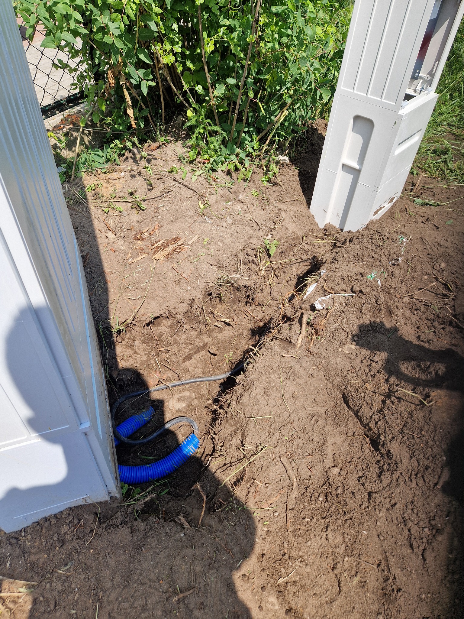 Przyłącze kabla w karbowanej rurze do białej skrzynki elektrycznej w ziemi, widok z góry, kabel zakopany w ziemi.