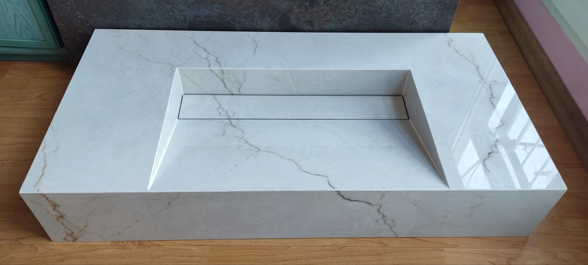 Blat umywalkowy z białego marmuru z minimalistycznym odpływem liniowym na drewnianej podłodze, ukazujący precyzję wykonania i nowoczesny design.