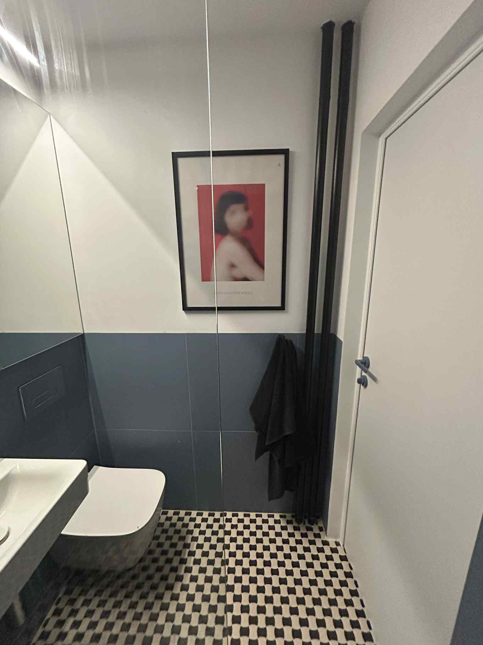 Nowoczesna łazienka z umywalką, toaletą, grzejnikiem żeberkowym i wzorzystą podłogą. Na ścianie wisi obraz w czarnej ramie.