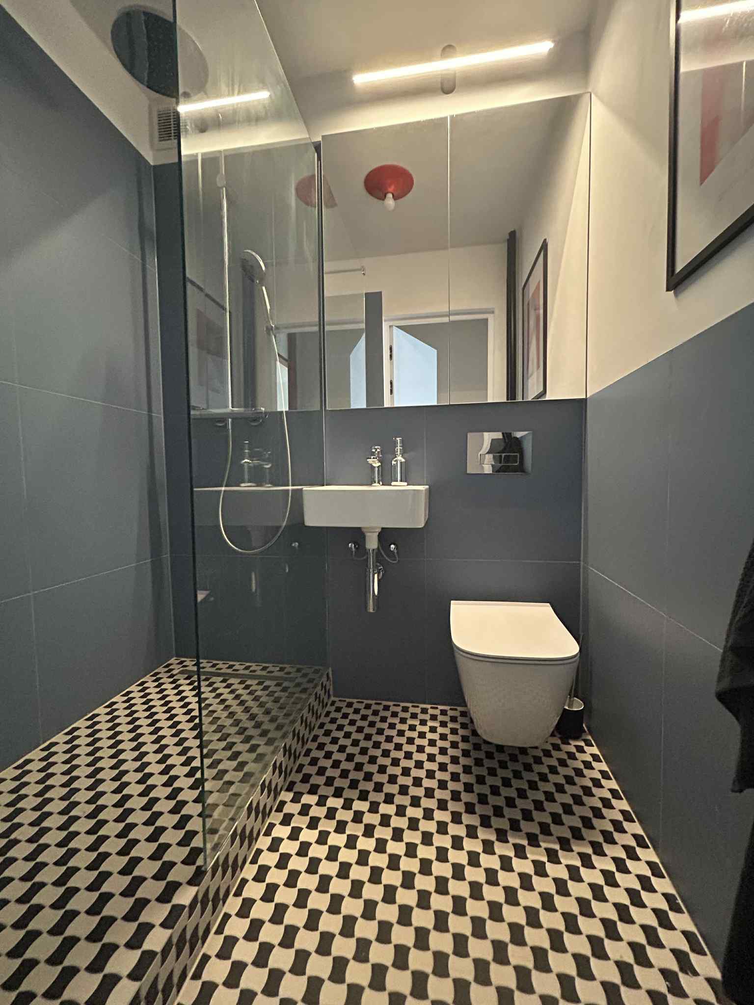 Nowoczesna łazienka z kabiną prysznicową, umywalką i toaletą w odcieniach szarości z czarno-białą wzorzystą podłogą. Lustro z oświetleniem LED.