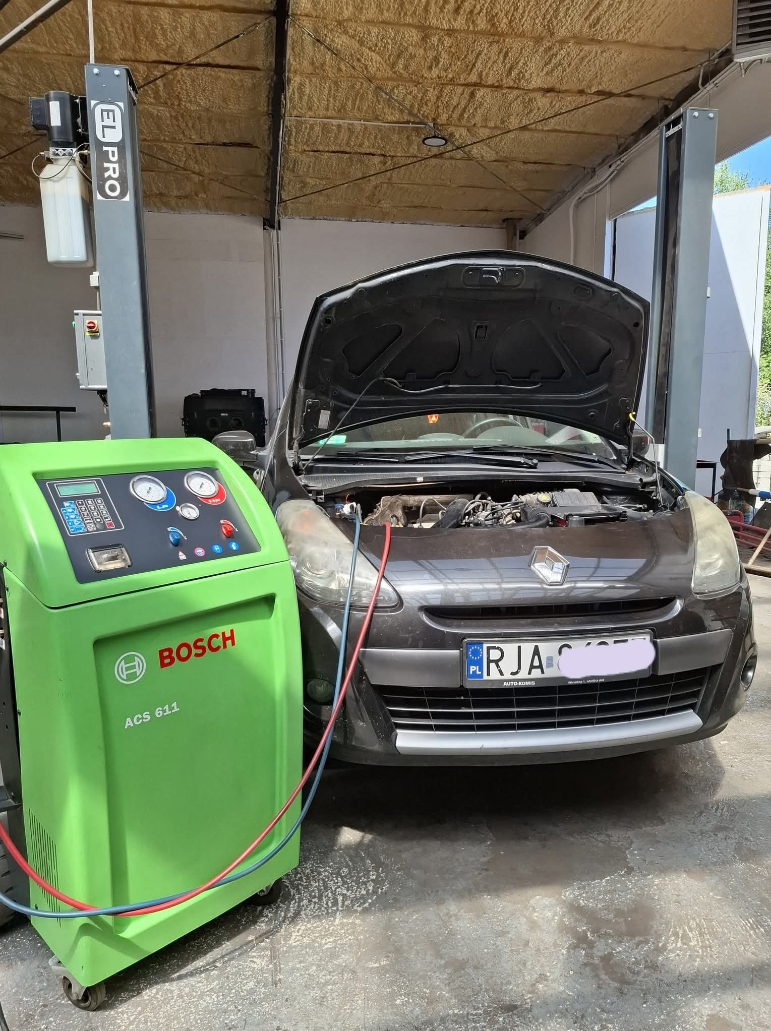 Samochód z otwartą maską podłączony do zielonego urządzenia Bosch ACS 611 w warsztacie, prawdopodobnie podczas serwisu klimatyzacji.