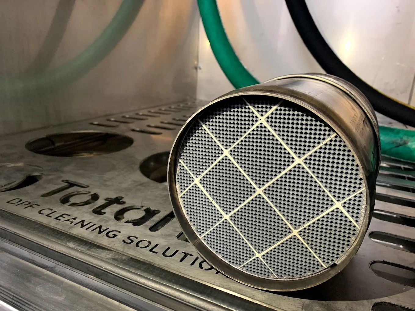 Filtr DPF po czyszczeniu, widoczna struktura wkładu z siatką. Metalowa obudowa i napis 'Total DPF Cleaning Solution' na tle.