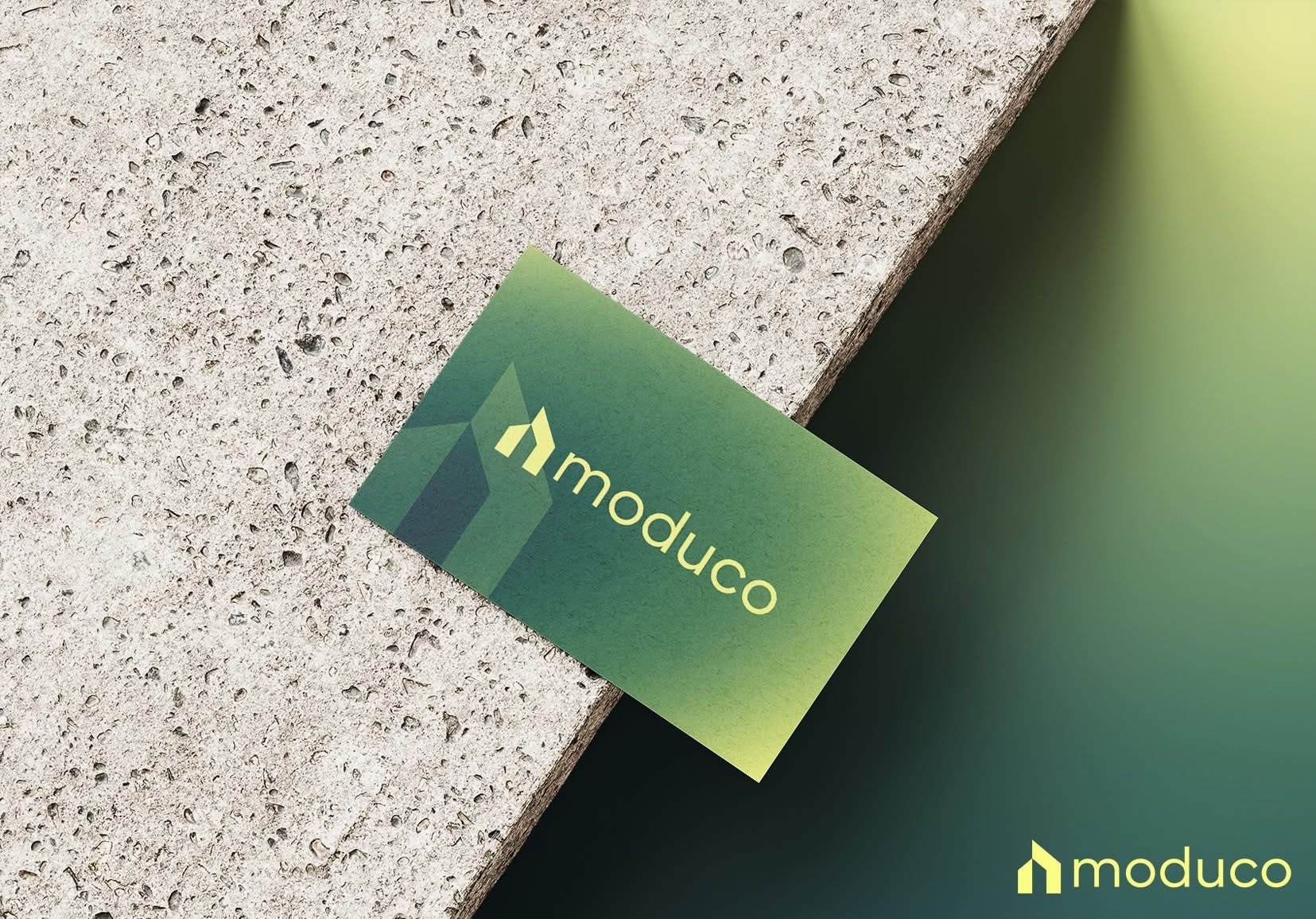 Żółto-zielona wizytówka z logo 'moduco' leży na szorstkiej, betonowej powierzchni, częściowo oświetlona gradientowym światłem.
