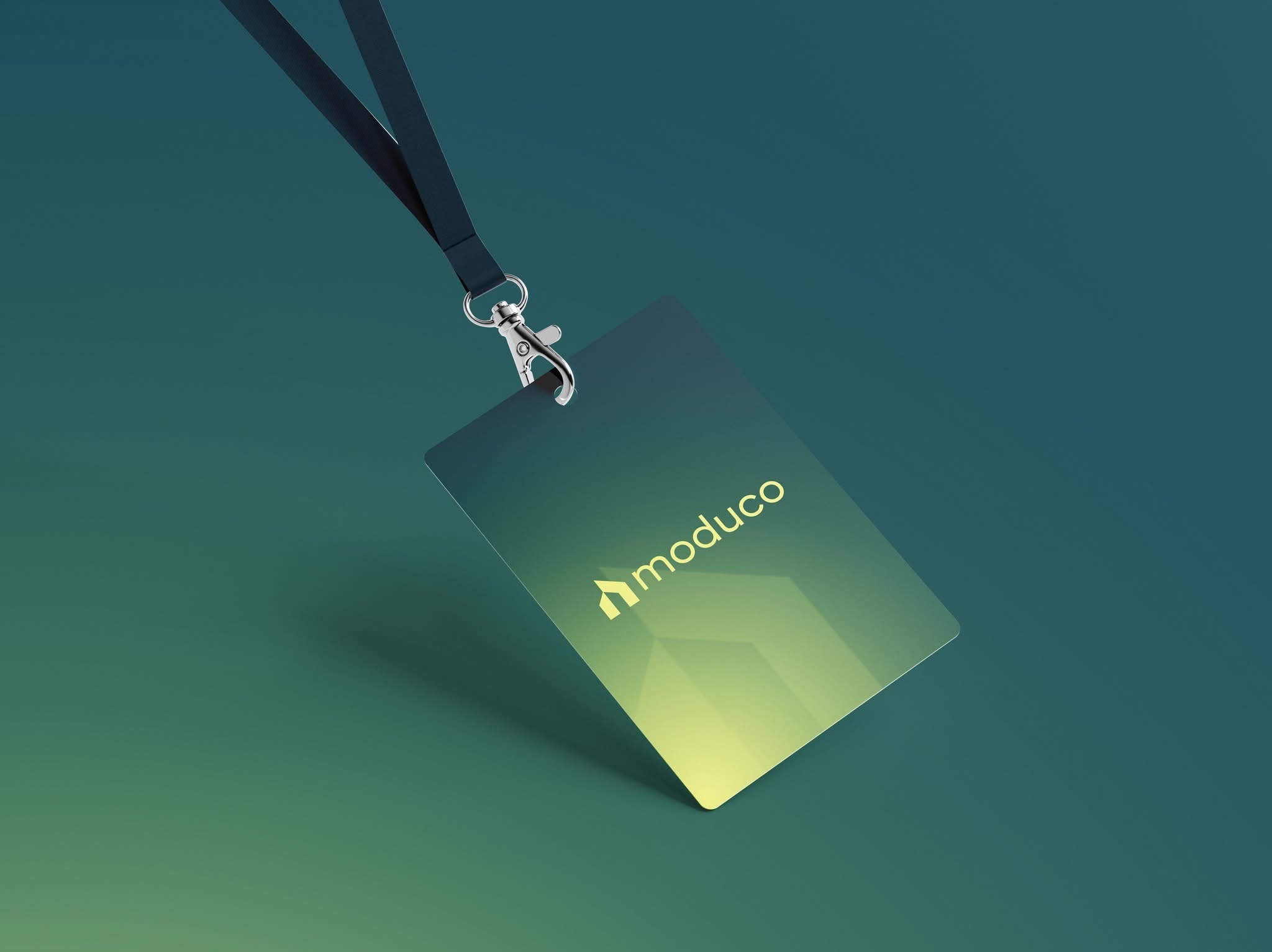 Identyfikator z logo 'moduco' zawieszony na smyczy, z gradientem od zieleni do żółci, leżący na zielonym tle. Metalowy karabińczyk i teksturowana smycz.