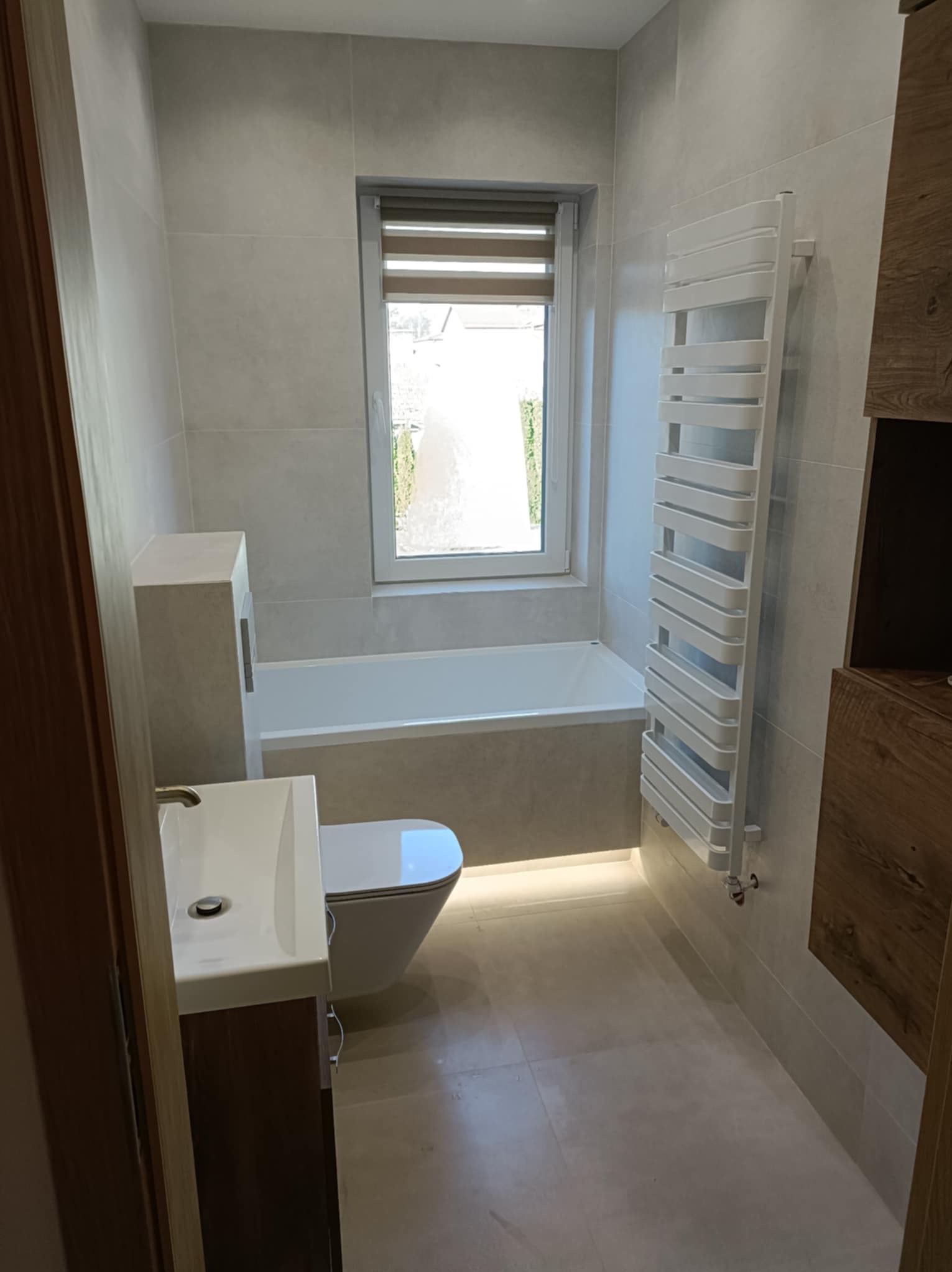 Jasna łazienka z wanną, umywalką i grzejnikiem drabinkowym. Uwagę przykuwa podświetlenie pod wanną i minimalistyczny styl wykończenia.