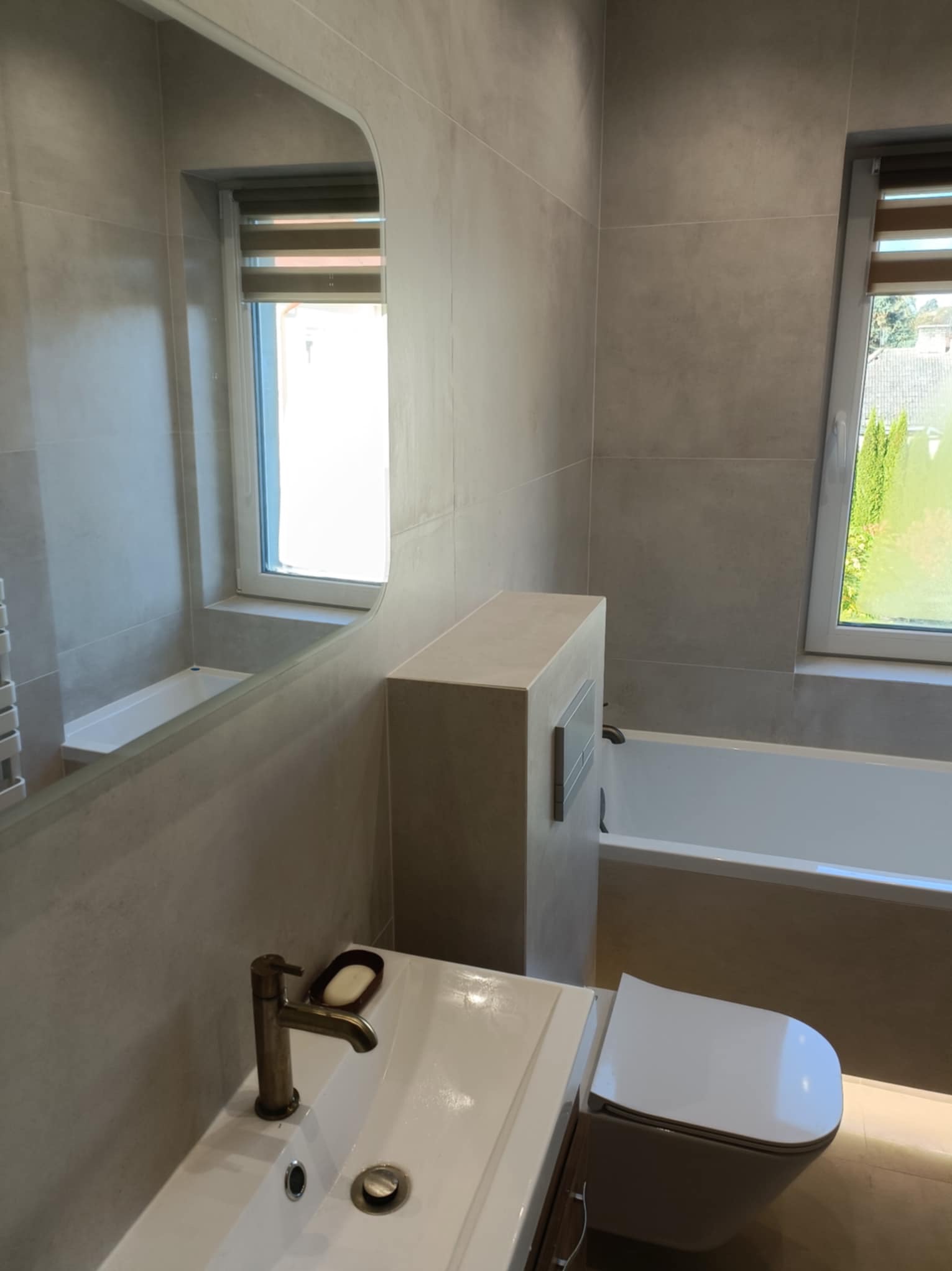 Nowoczesna łazienka w Puławach z beżowymi płytkami, umywalką z brązową armaturą i lustrem. Widoczna wanna i toaleta. Minimalistyczny design.