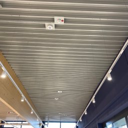 ZID-ELEKTRO PATRYK WASILEWSKI - Metalowy sufit z zamontowanymi reflektorami szynowymi i czujnikami dymu. Widok z dołu, oświetlenie w nowoczesnym wnętrzu komercyjnym.