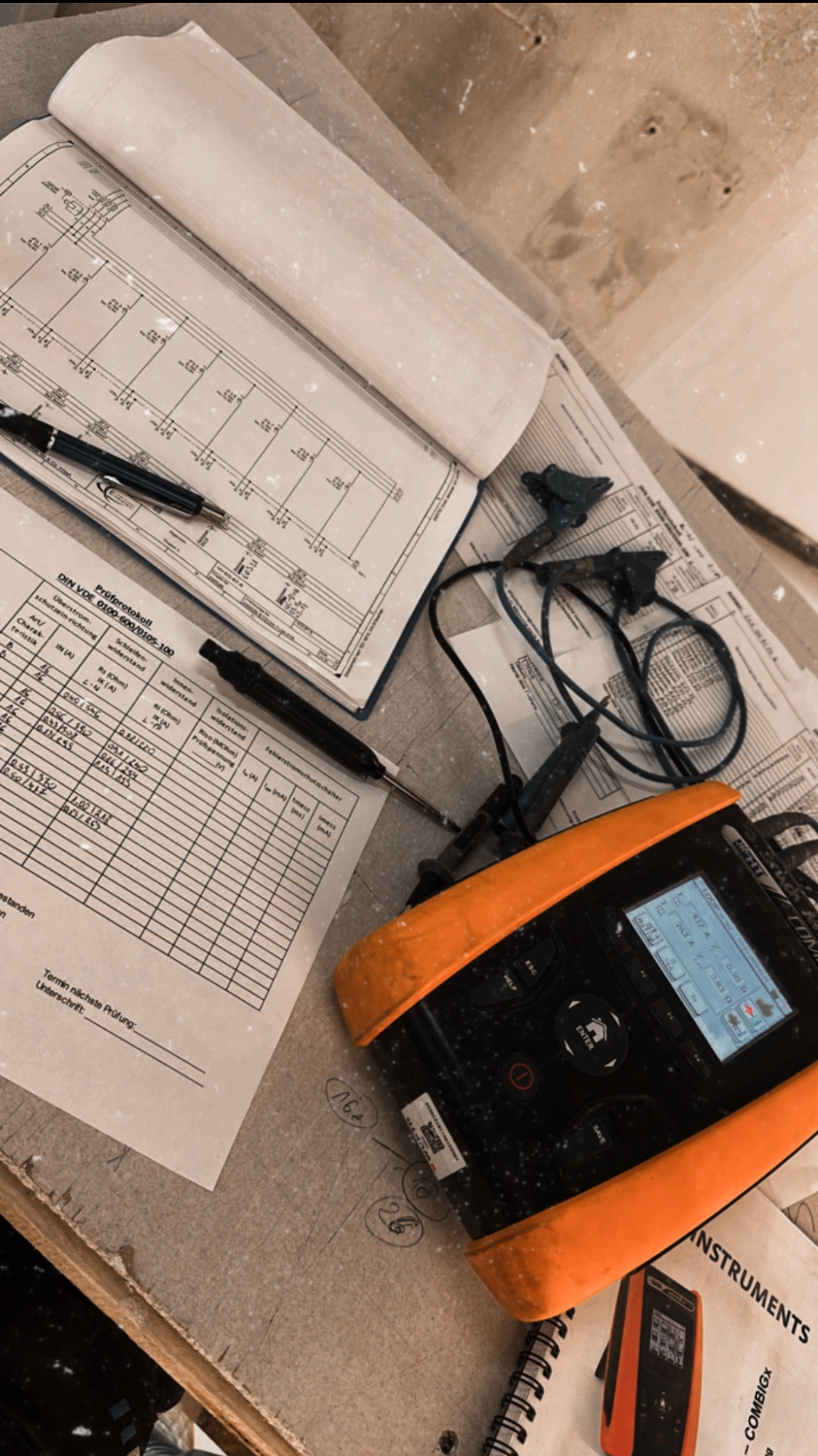 Miernik elektryczny, schemat instalacji i protokół pomiarowy na stole roboczym. Narzędzia i dokumentacja pomiarów elektrycznych w trakcie pracy.