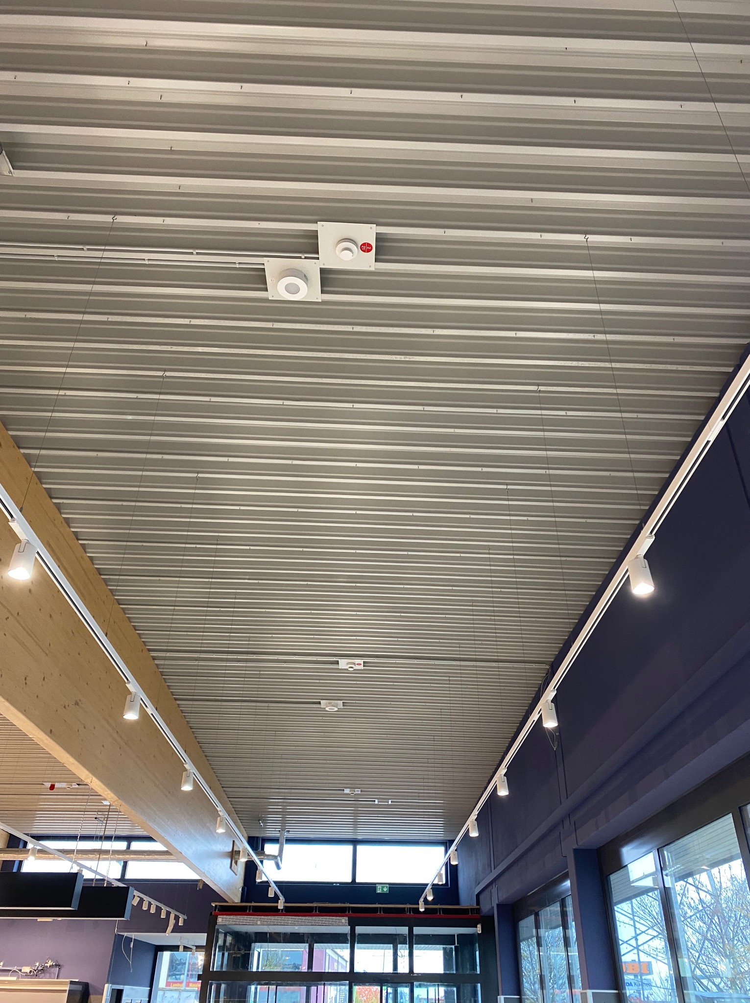 Metalowy sufit z zamontowanymi reflektorami szynowymi i czujnikami dymu. Widok z dołu, oświetlenie w nowoczesnym wnętrzu komercyjnym.