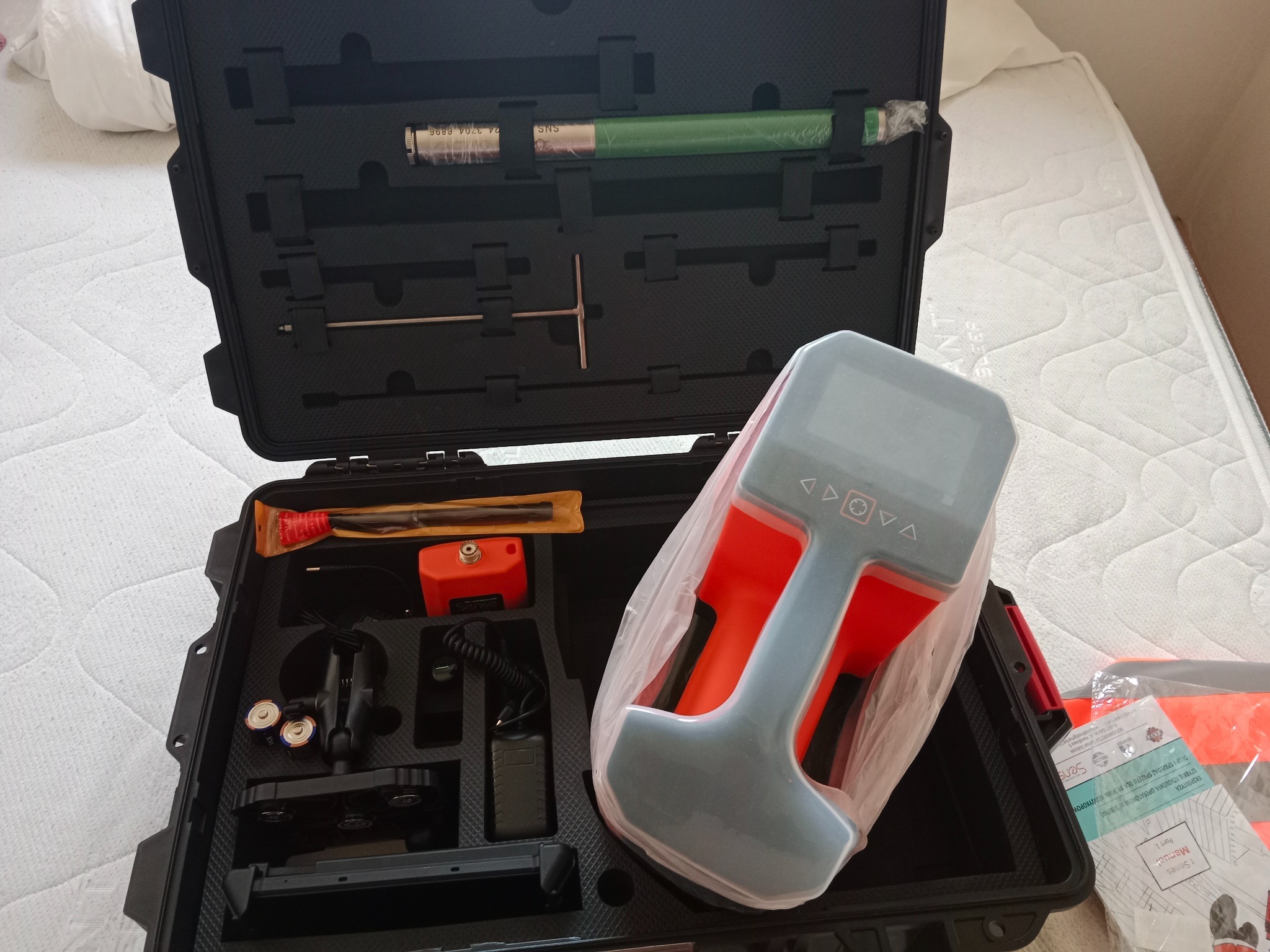 Zestaw narzędzi do precyzyjnych prac ziemnych w czarnej walizce: lokalizator, sondy, zasilacz, instrukcja. Białe tło.