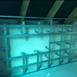 Metalowa konstrukcja stelażu pod płytę G-K na poddaszu, widoczne elementy mocujące i fragment instalacji sanitarnej Geberit.