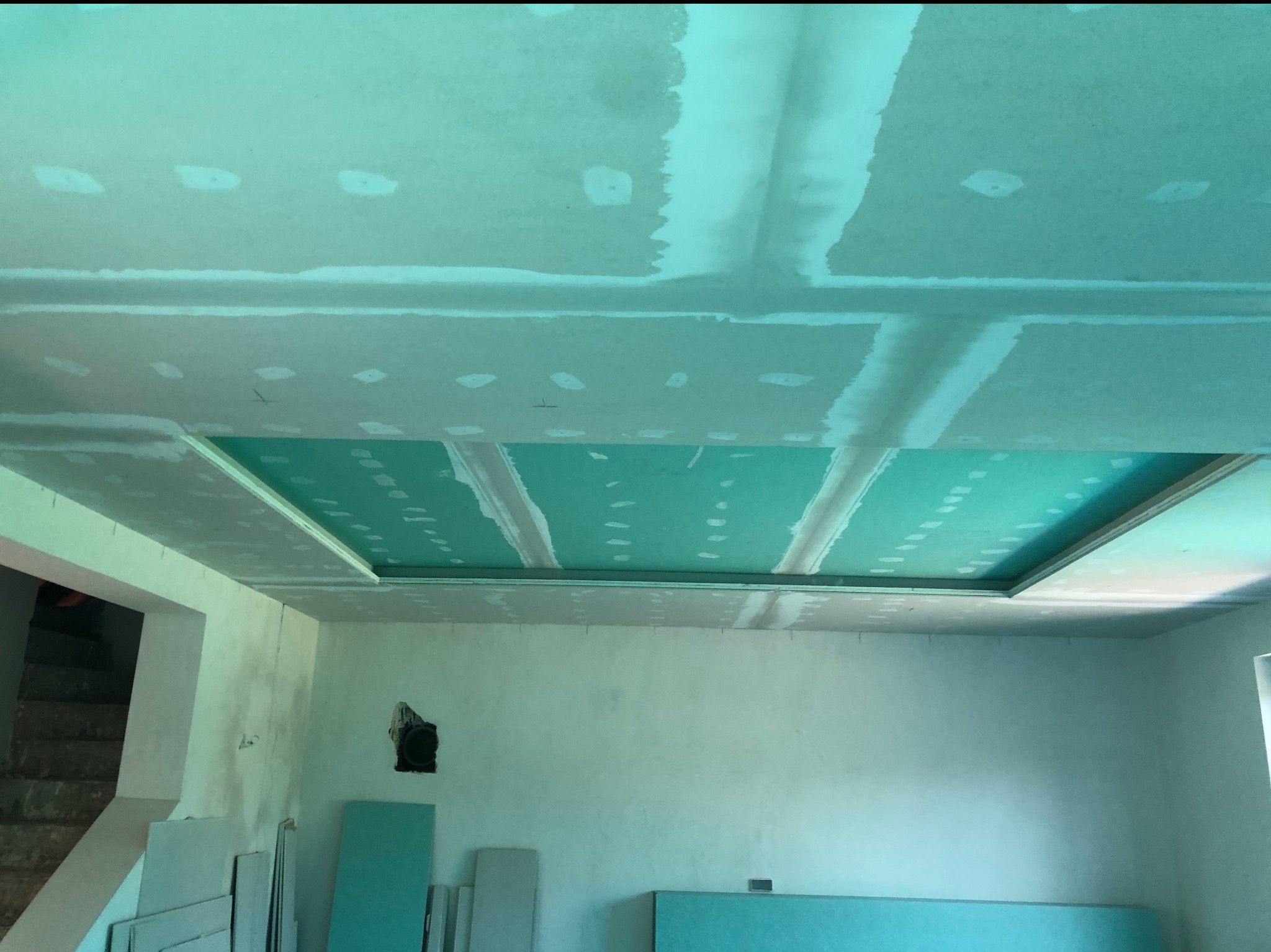 Sufit podwieszany z płyt karton-gips, częściowo zaszpachlowany, widoczne łączenia i płyty na podłodze. Prace wykończeniowe w nowym wnętrzu.