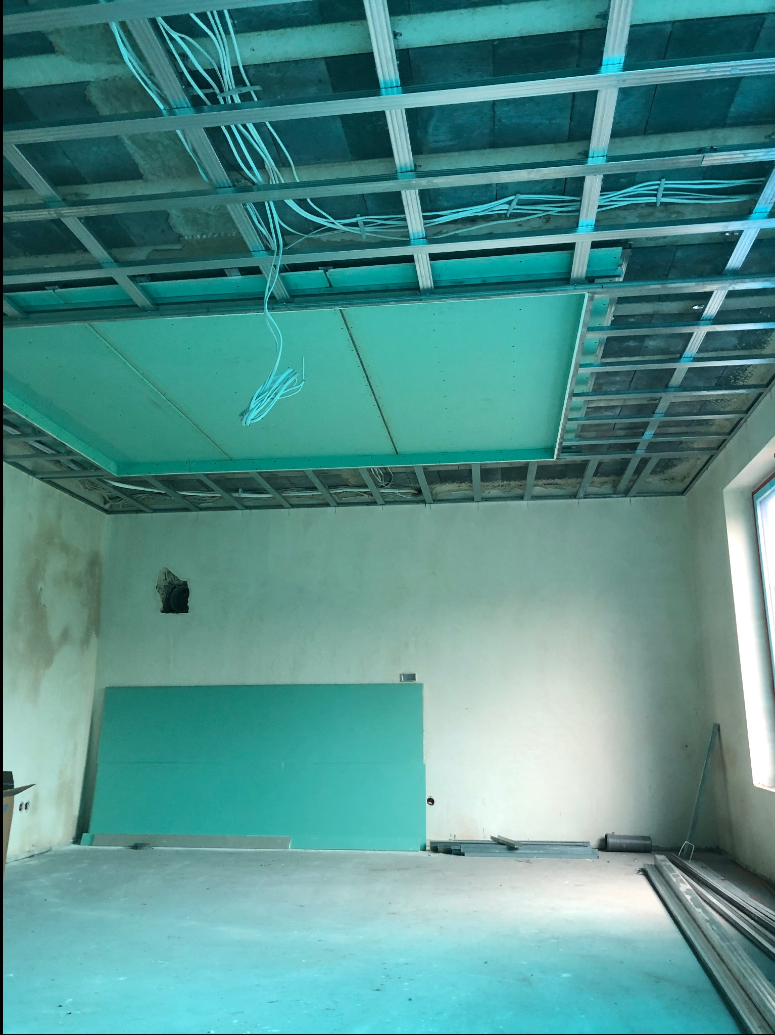Wnętrze w trakcie prac: częściowo zamontowana płyta gipsowa na suficie, widoczne kable i metalowy stelaż. Na podłodze płyta gipsowa i profile.