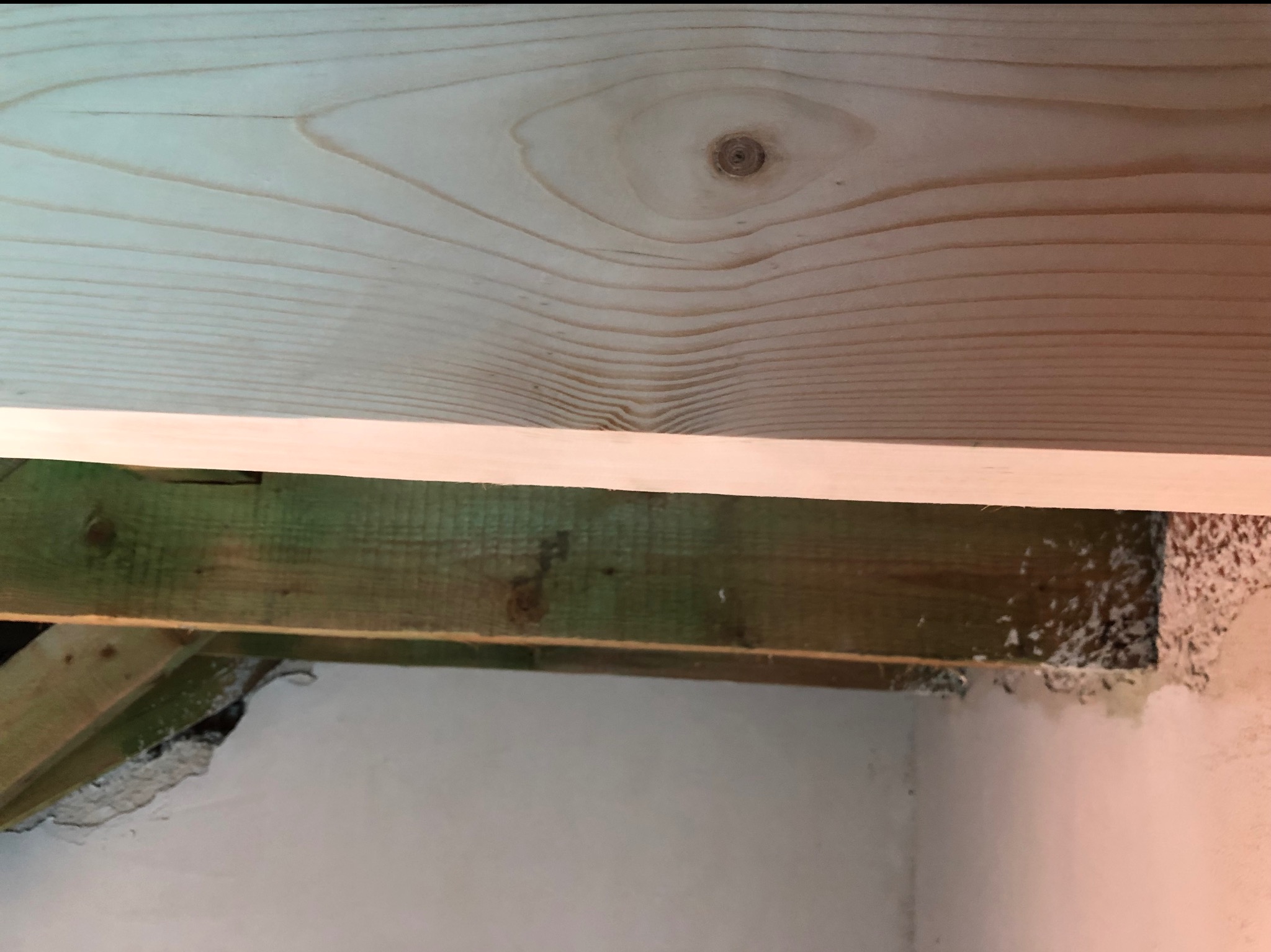 Drewniana konstrukcja sufitu z widocznymi belkami nośnymi i fragmentem ściany z ubytkami tynku, ukazująca etap prac wykończeniowych w pomieszczeniu.