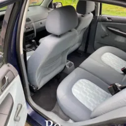 Wnętrze samochodu po czyszczeniu: jasnoszare fotele z subtelnym wzorem, otwarte drzwi ukazują czystą tapicerkę, widoczne detale wnętrza.