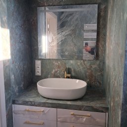 Davit Mnatsakanyan - Wykończona łazienka z umywalką nablatową, złotą armaturą i marmurowymi płytkami w odcieniach zieleni. W lustrze odbija się grzejnik drabinkowy i osoba robiąca zdjęcie.