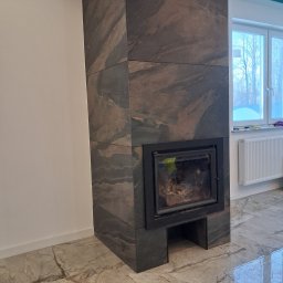 Da-Li HOM BUILDER - Obudowa kominka z kamienia naturalnego o wyraźnym wzorze żyłkowania, dopasowana do marmurowej podłogi. W tle okno z widokiem na zimowy krajobraz.