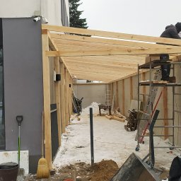 Davit Mnatsakanyan - Budowa drewnianej konstrukcji zadaszenia przy budynku restauracji w zimowej scenerii. Pracownik na rusztowaniu montuje elementy. Widoczne narzędzia i materiały budowlane.