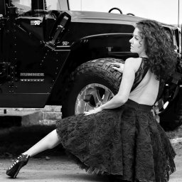 Przemek Paszkiewicz Pasja Obiektywu - Czarno-białe zdjęcie kobiety w sukience pozującej przy czarnym Hummerze. Kobieta siedzi bokiem, z głową odwróconą w lewo. Sukienka z koronkowym wzorem.
