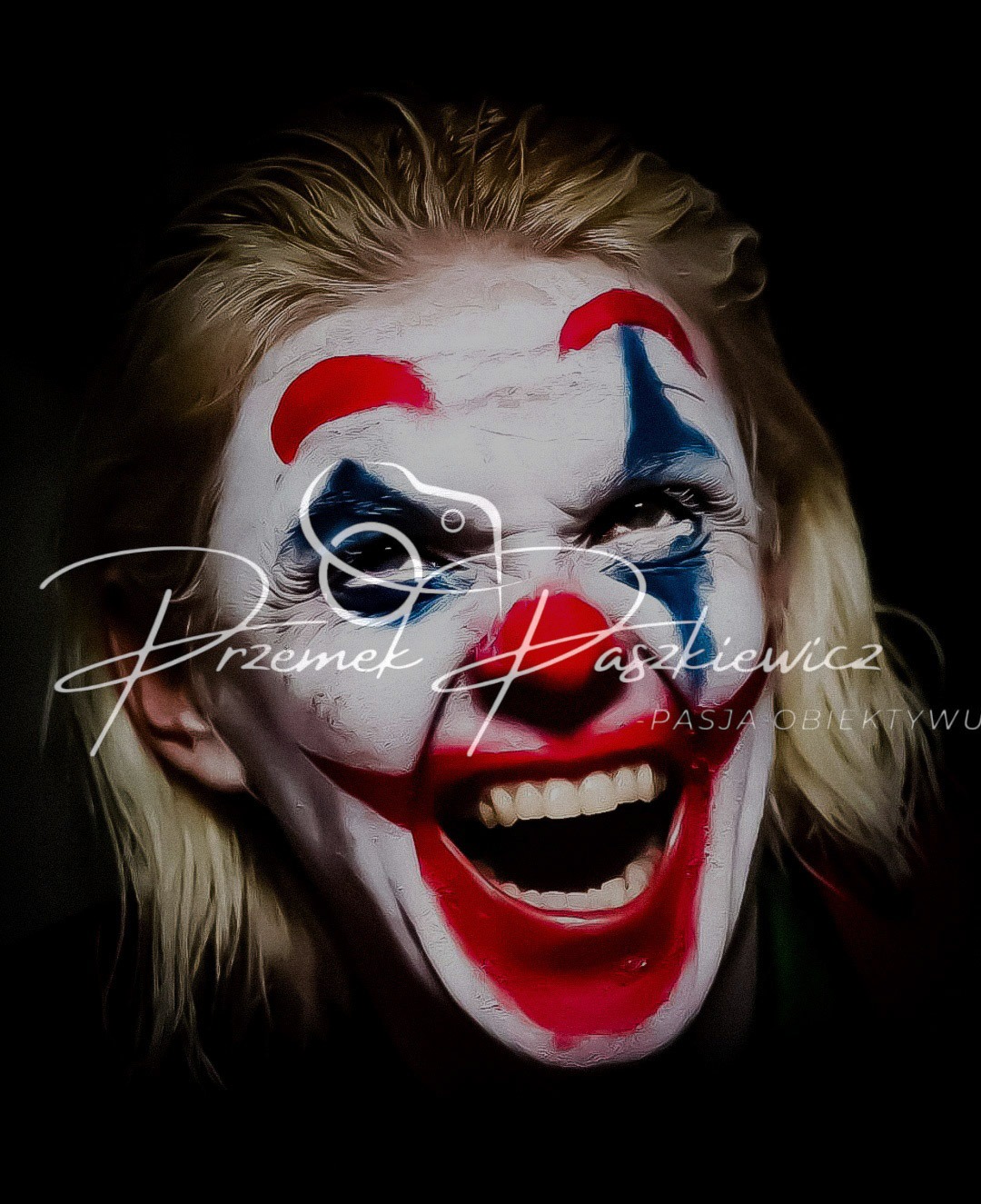 Portret kobiety w makijażu inspirowanym Jokerem, z intensywnym wyrazem twarzy, na ciemnym tle. Widoczny autorski podpis fotografa.